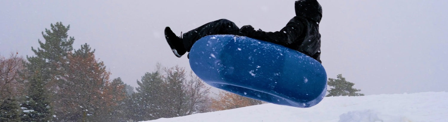 Lakesurf Skookum Tube Ultimate Two-in-One River and Snow Towable Tube. Adult jumping off snow hill on blue tube.